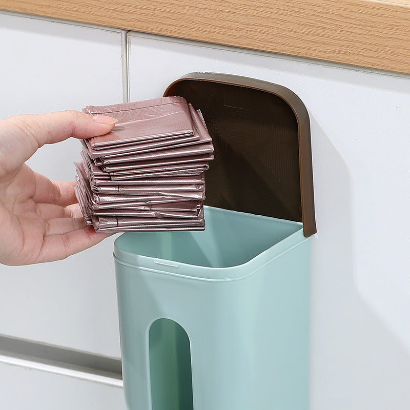 Hand placing folded grocery bags into the top of a green wall-mounted dispenser